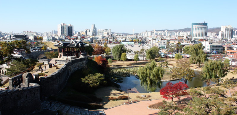 image Part of the Hwaseong Fortress, next to a garden and Suwon in the Background